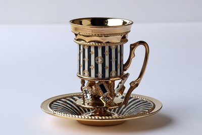 紺と白の縦縞の胴に金の紋と星を描き、宝石の脚を付けたカップ＆ソーサー
