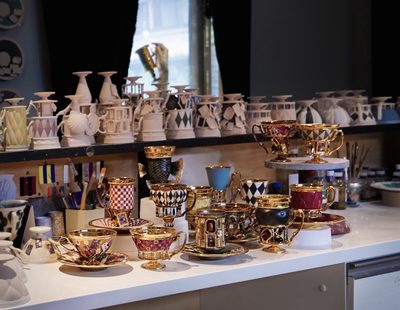 工房の机に並ぶ、仕上げたカップ＆ソーサーやマグと、棚に並ぶ素焼きの器
