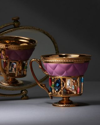ピンクのキルト模様の胴に、金の柱の輪と色とりどりの宝石を付けたカップ。丸い鏡に、もう1点が映る